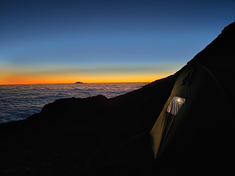 Coucher de soleil spectaculaire au-dessus d'une mer de nuages avec une tente au premier plan.