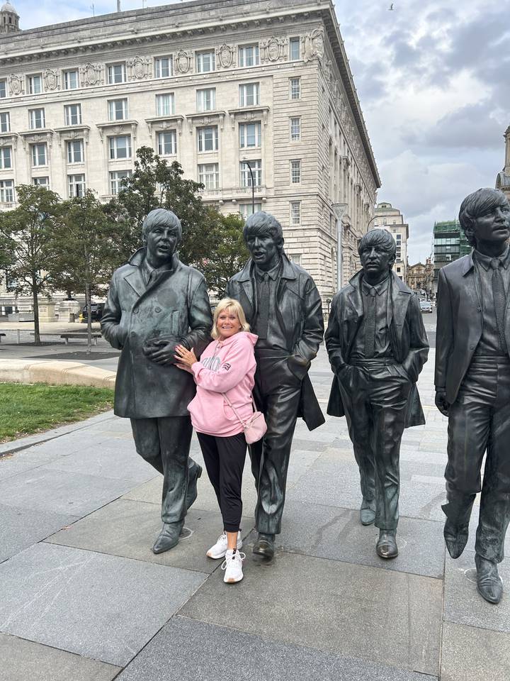 Statues de quatre hommes et une personne posant avec elles. Grand bâtiment en arrière-plan.