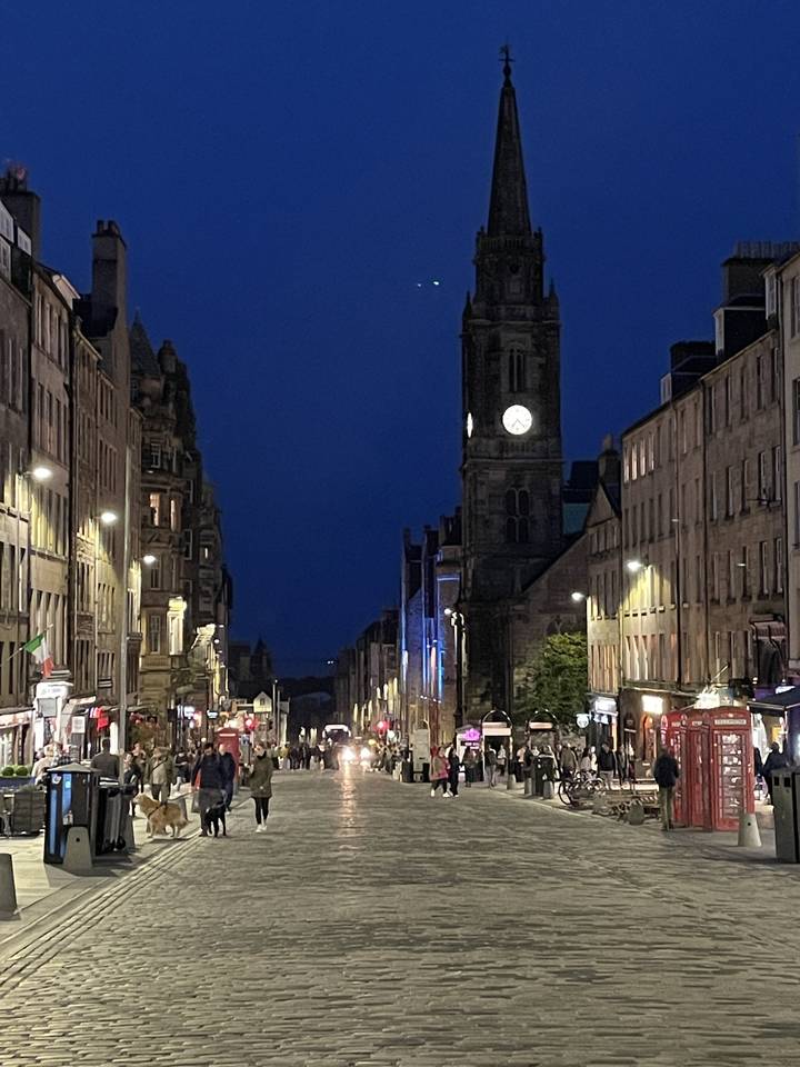 Vue de rue la nuit, bâtiments éclairés et gens se promenant sur une rue pavée.