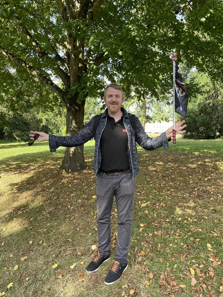 Un individu posant avec une canne sous des arbres.