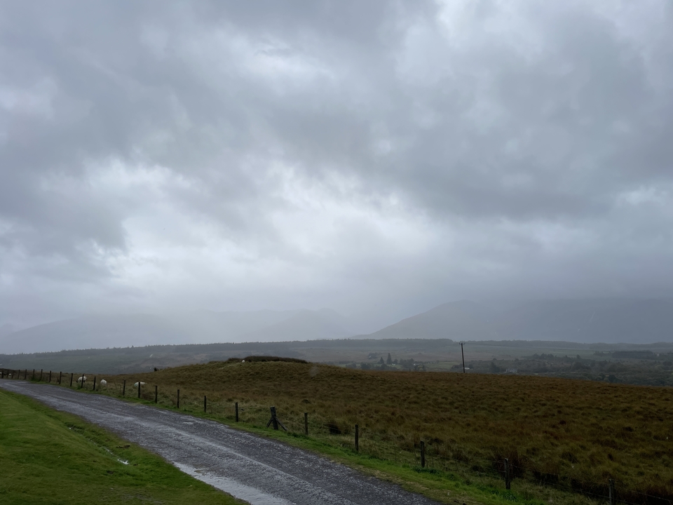 Paysage nuageux avec des montagnes lointaines et des champs herbeux.