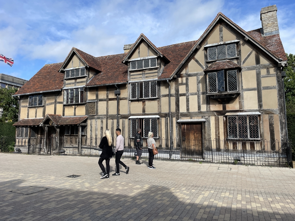 Des gens qui passent devant un bâtiment historique à colombages, avec un drapeau qui flotte au sommet.