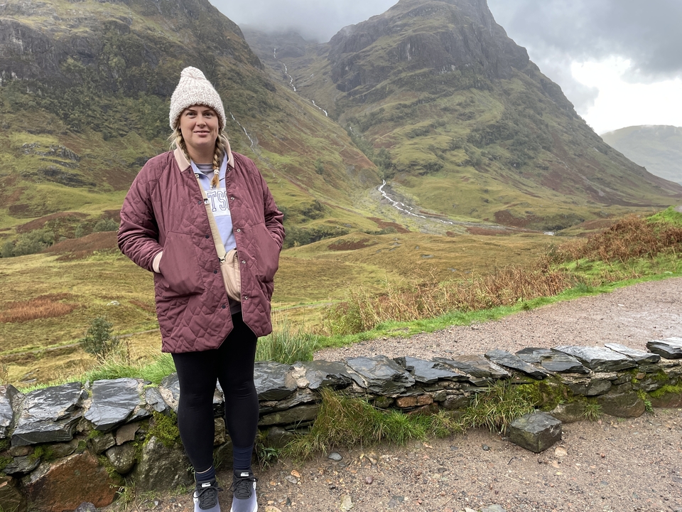 Une personne debout dans une région montagneuse avec un mur de pierre.
