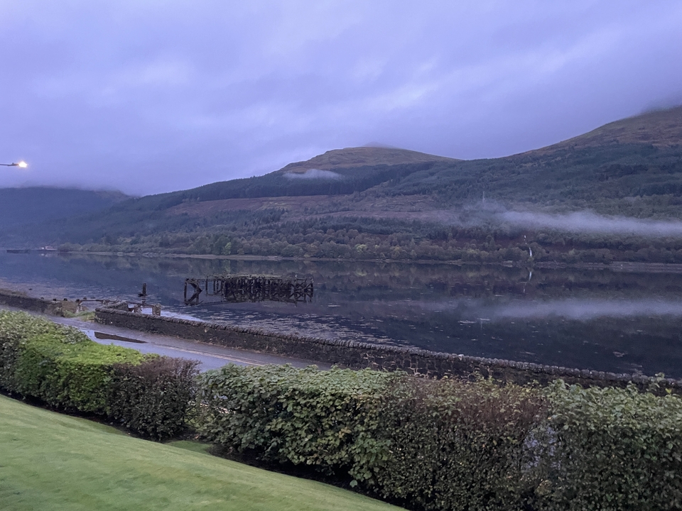 Un paysage tranquille avec un plan d'eau calme, entouré de collines et de zones boisées sous un ciel dégagé.
