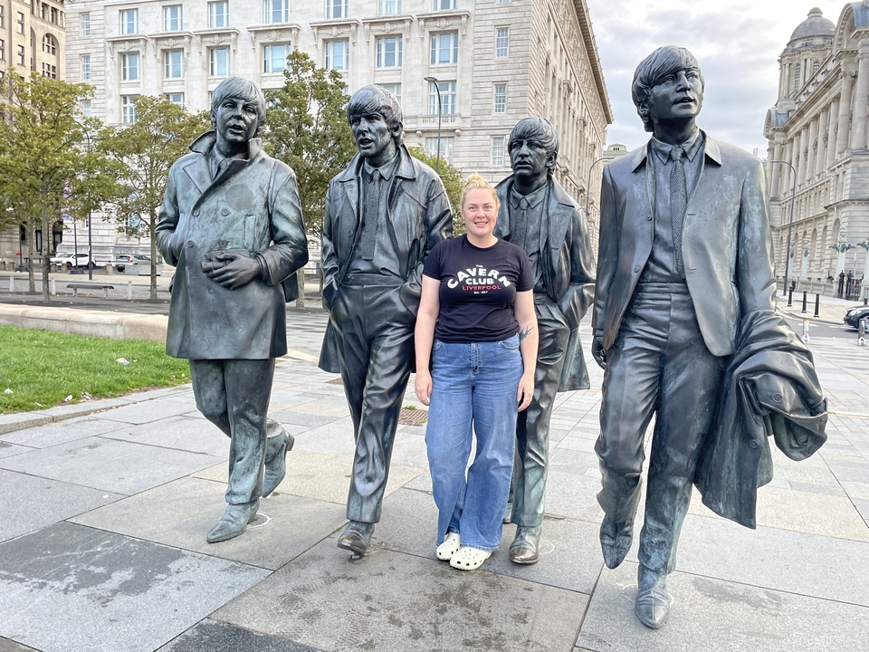 Une personne posant à côté de statues représentant des icônes musicales.