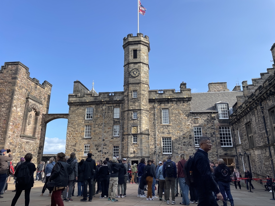 Un grand bâtiment en pierre avec une tour d'horloge, des gens rassemblés devant.