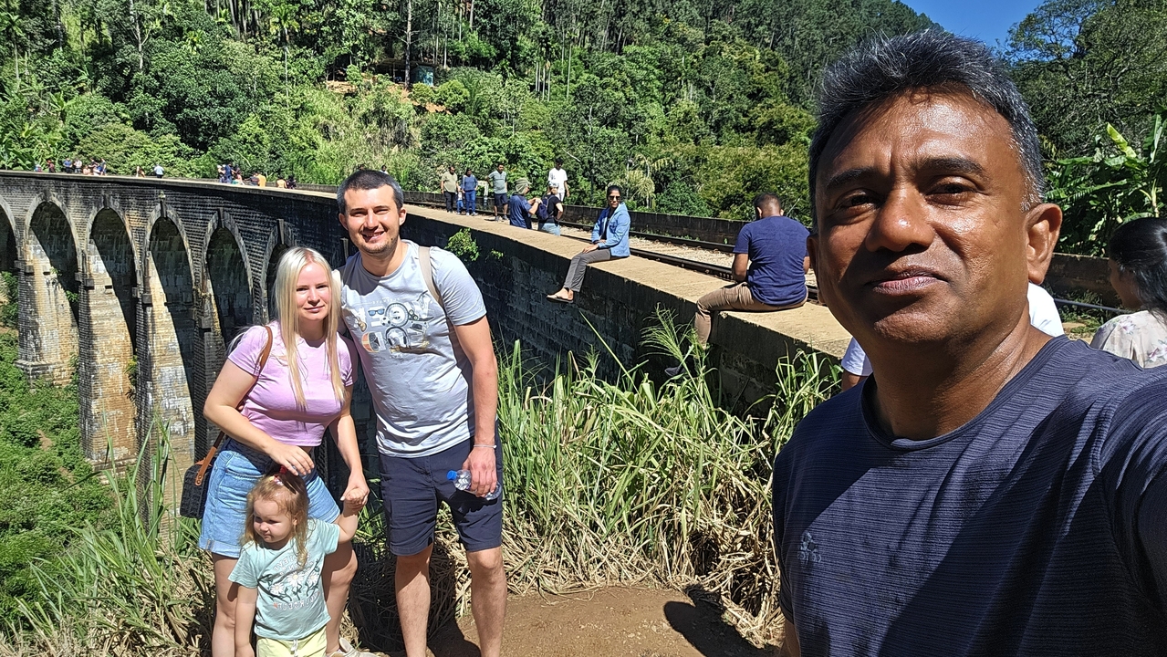 Groupe de personnes posant près d'un pont ferroviaire dans un cadre verdoyant luxuriant.