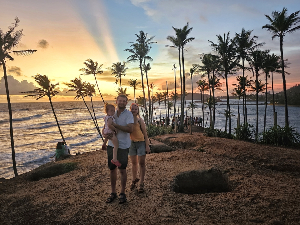 Famille profitant d'un coucher de soleil sur une plage avec des palmiers.