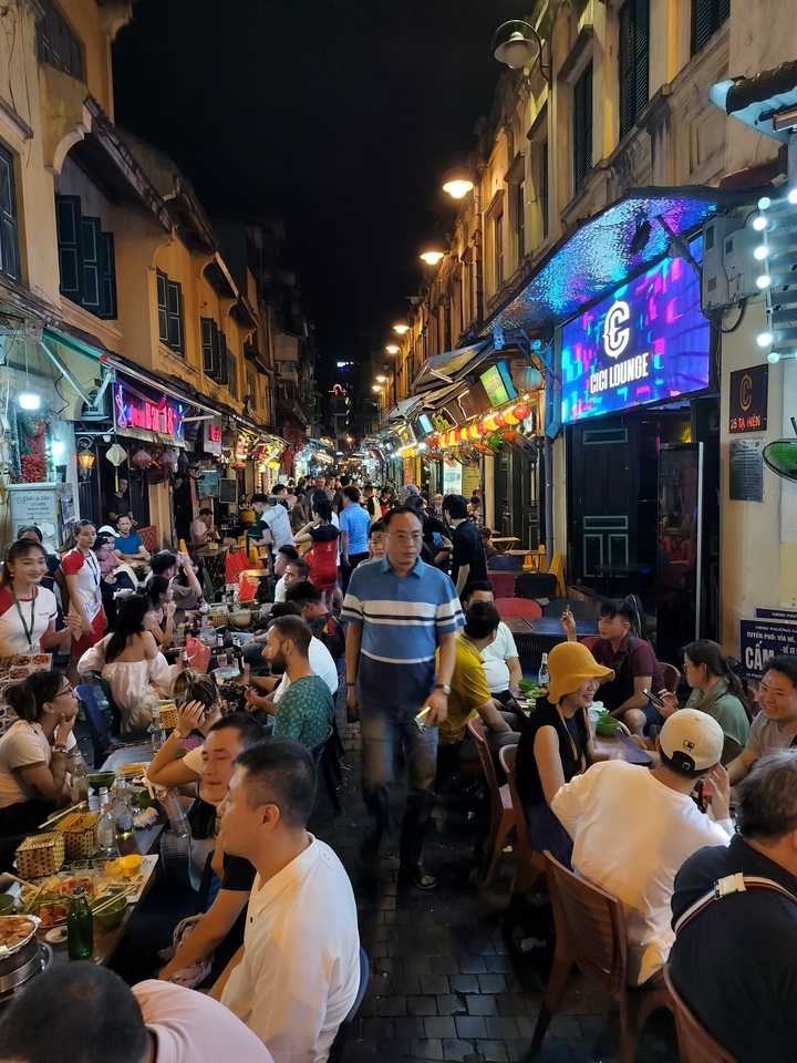Scène de marché nocturne en plein air bondé avec divers magasins et des gens.