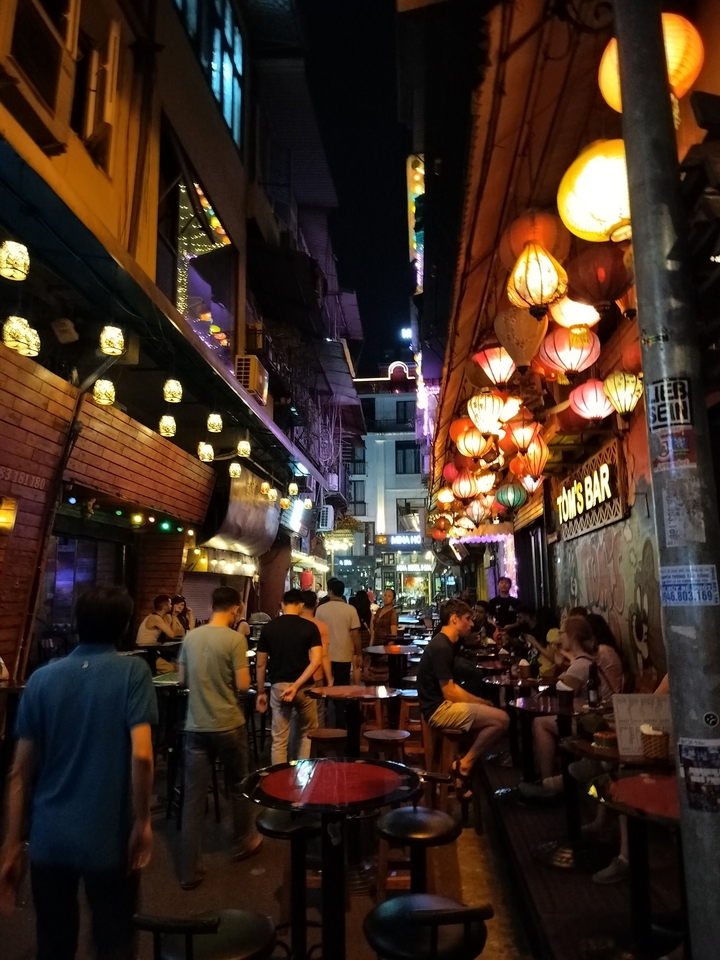Scène de rue animée la nuit avec des lanternes colorées et des gens.