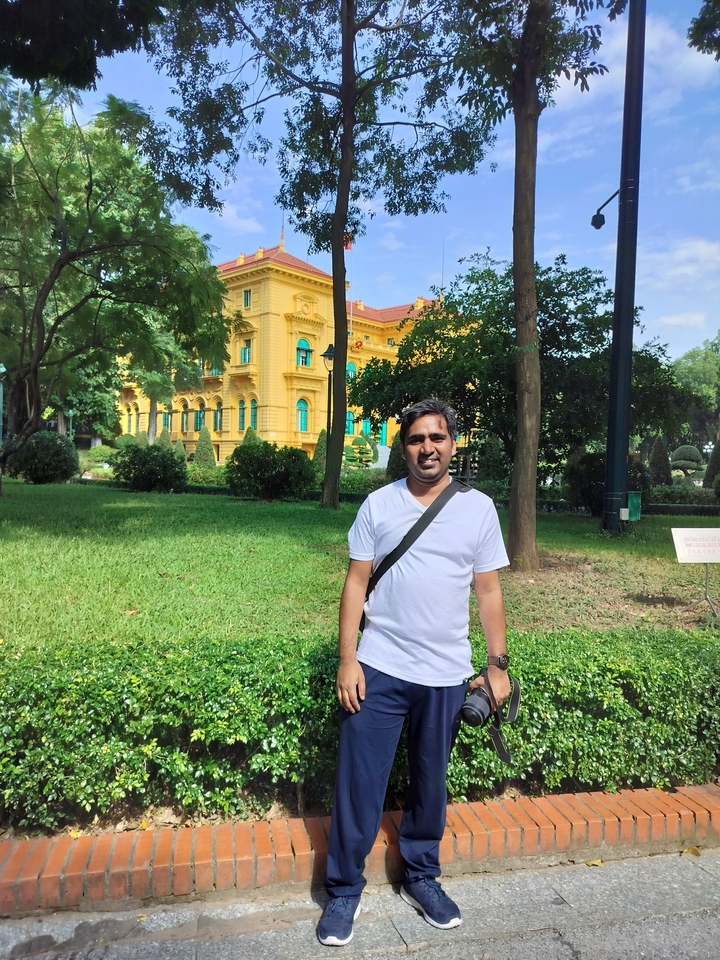 Personne debout dans un parc devant un bâtiment de style colonial jaune.