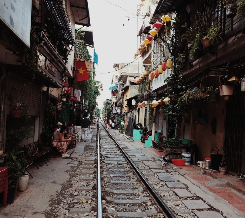 Rue étroite bordée de cafés, de plantes et de lanternes colorées.