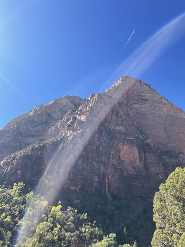 Tall sandstone cliff with sunlight casting a lens flare.