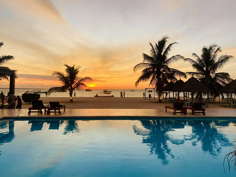 Coucher de soleil sur une plage avec des palmiers et une piscine.
