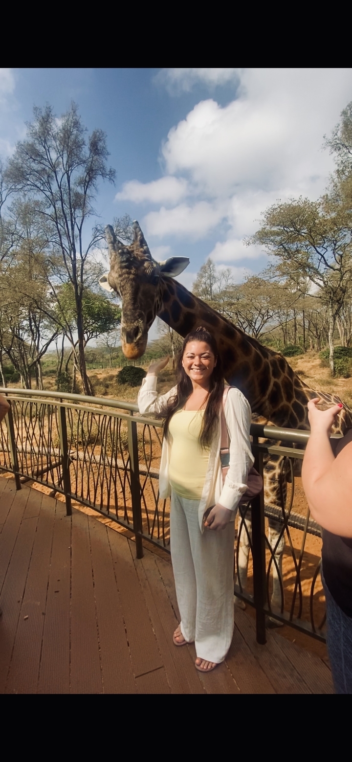 Personne posant à côté d'une girafe derrière une clôture.