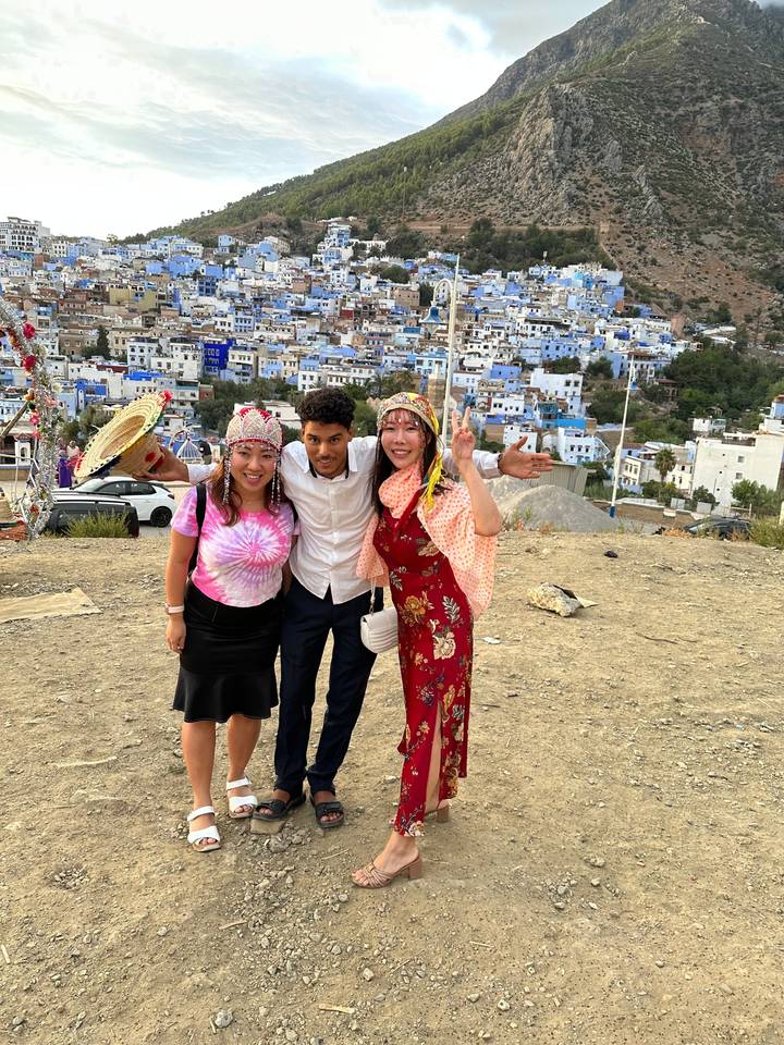 Trois personnes en tenue colorée devant une ville bleue sur une colline.