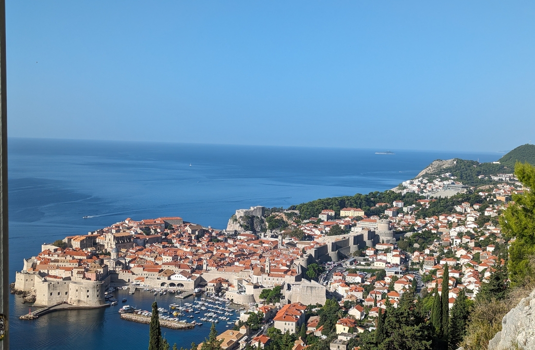 Vue panoramique d'une ville côtière avec des fortifications historiques et une mer bleue.