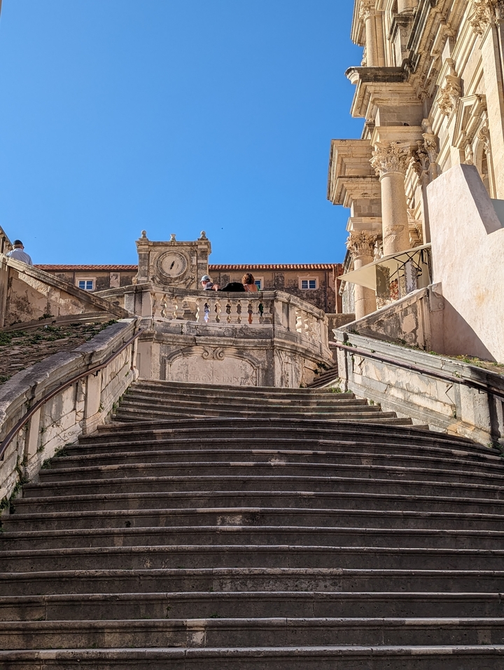 Escalier en pierre menant à un bâtiment ancien avec des touristes qui montent.