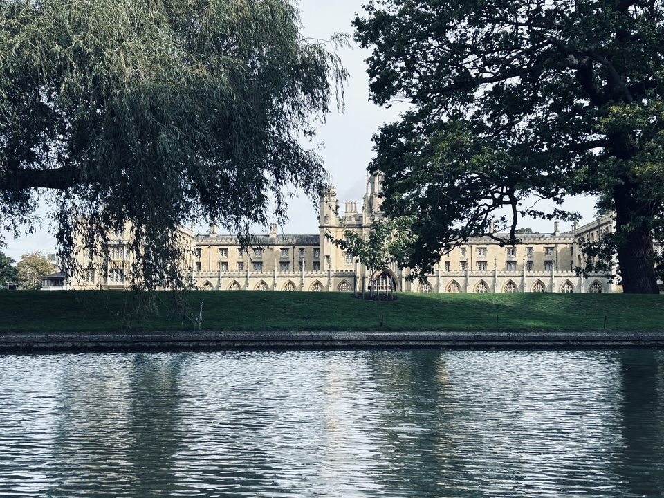 Un grand bâtiment historique vu à travers les arbres de l'autre côté d'une rivière.