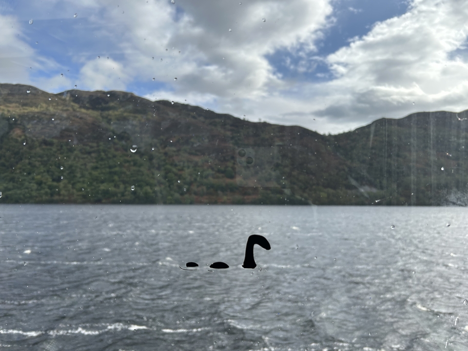 Le Loch Ness avec des montagnes en arrière-plan, et une silhouette de Nessie sur la fenêtre.