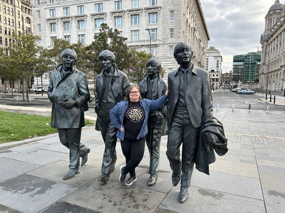 Une personne posant avec des sculptures des Beatles sur une place de la ville.