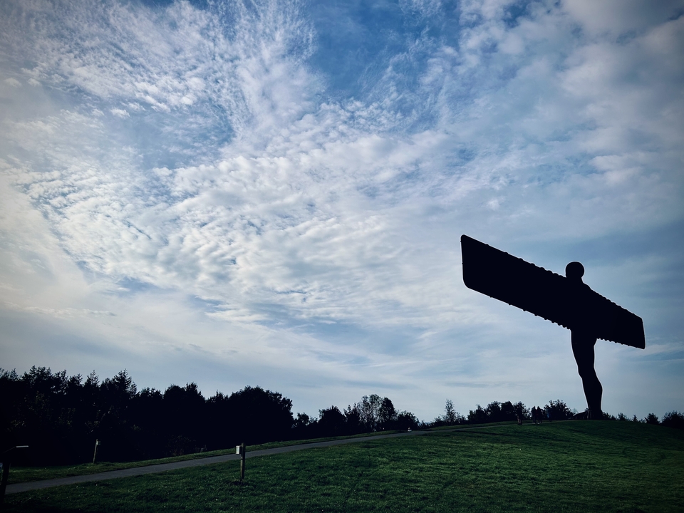 Silhouette d'une grande statue d'ange contre un ciel nuageux.