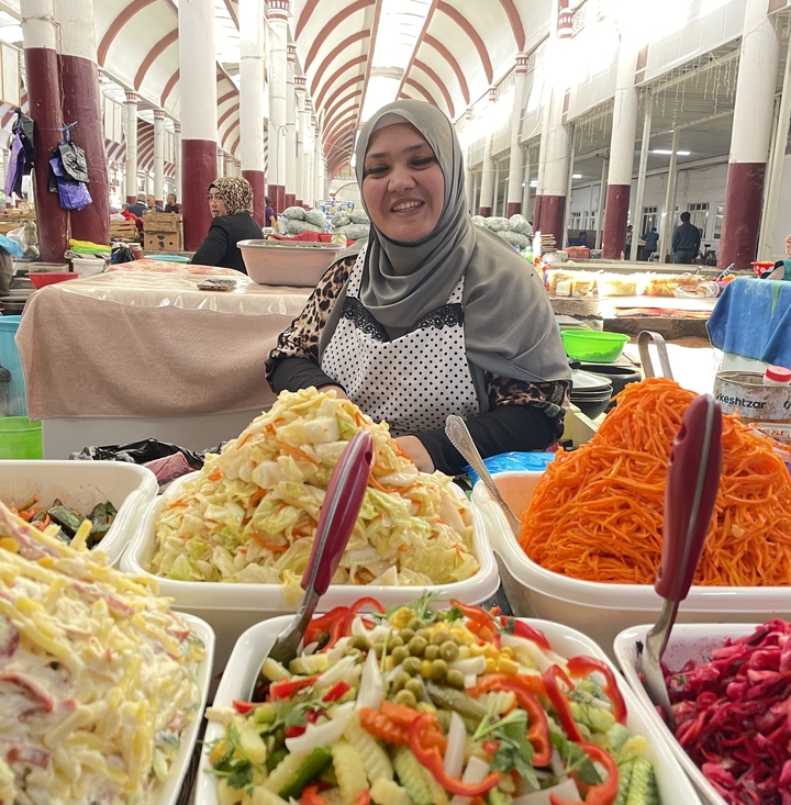 Una mujer en un puesto del mercado vendiendo verduras en escabeche en cuencos.