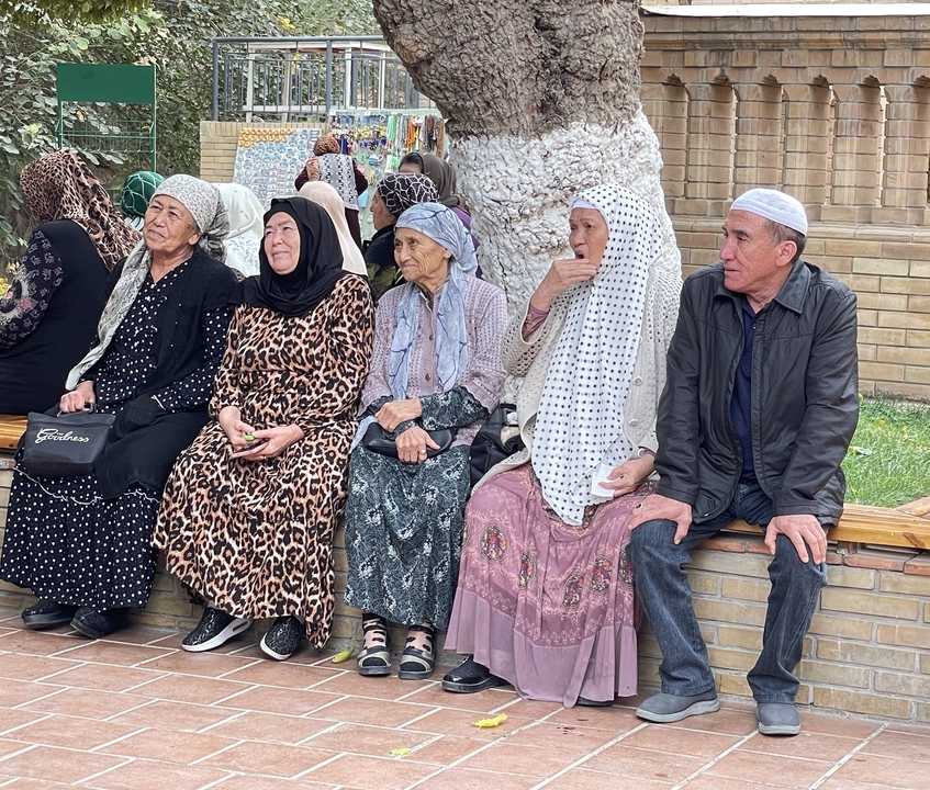 Un grupo de personas mayores sentadas en un banco con vestimenta tradicional.