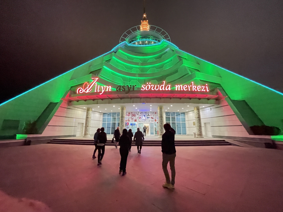 Personas caminando hacia un edificio con forma de pirámide con luces de neón.