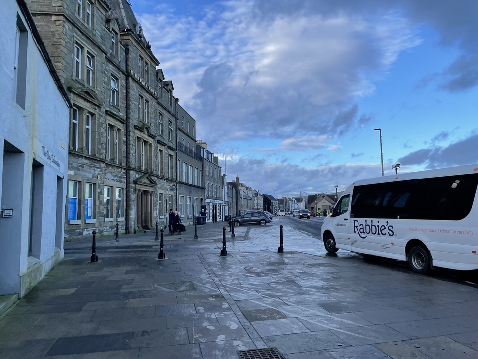 Rue avec de vieux bâtiments en pierre et un autocar de tourisme garé.