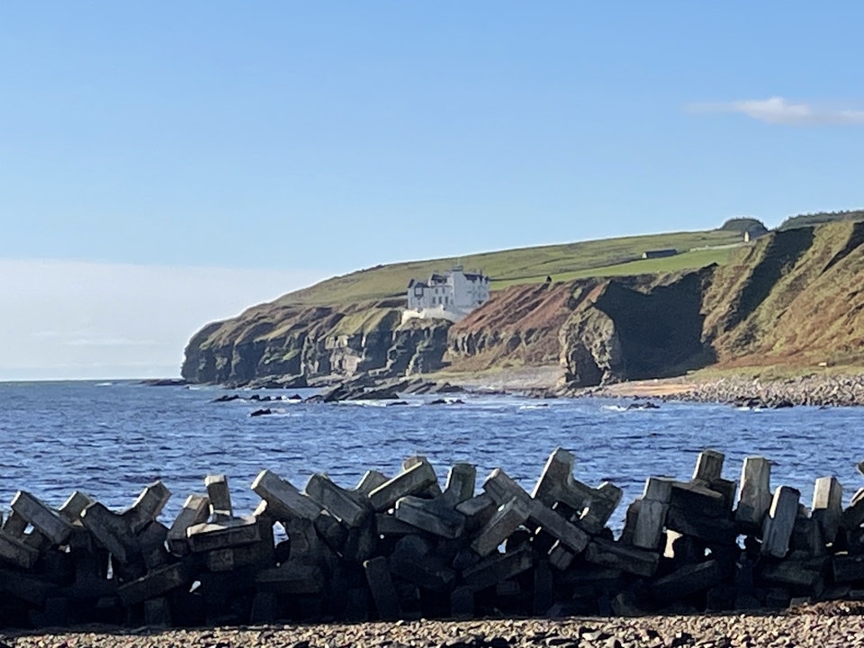 Falaises côtières avec un bâtiment blanc et mer agitée.