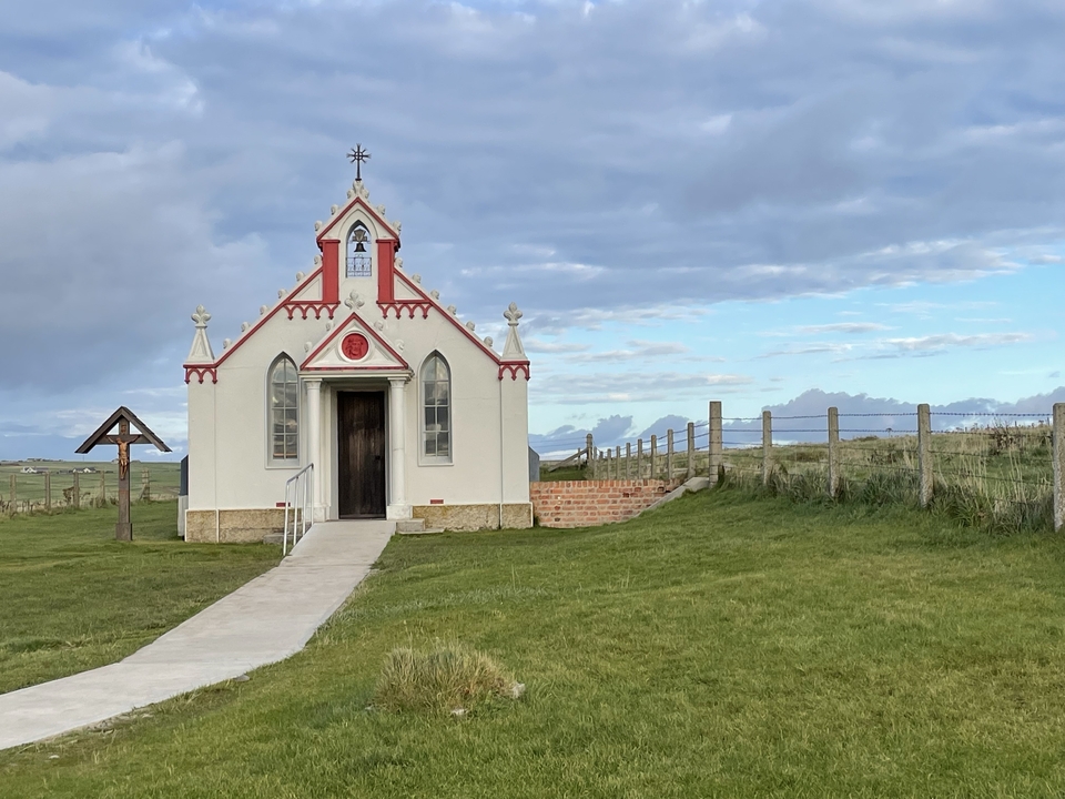Petite chapelle blanche dans un champ herbeux.