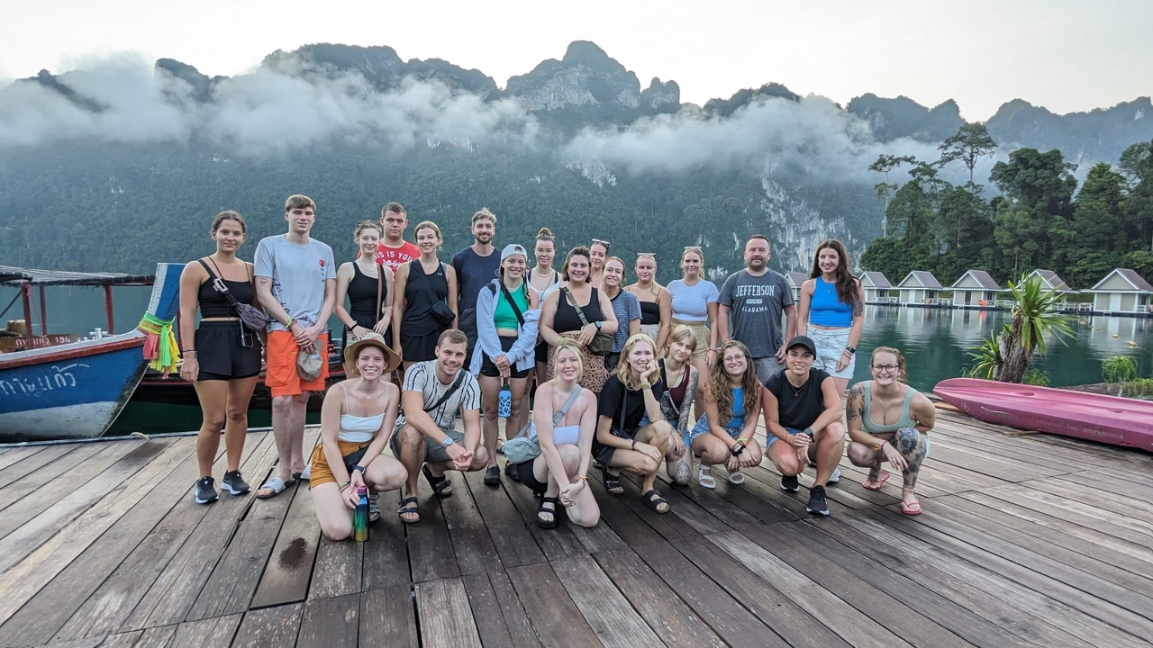Grupo de personas en un muelle con montañas detrás.