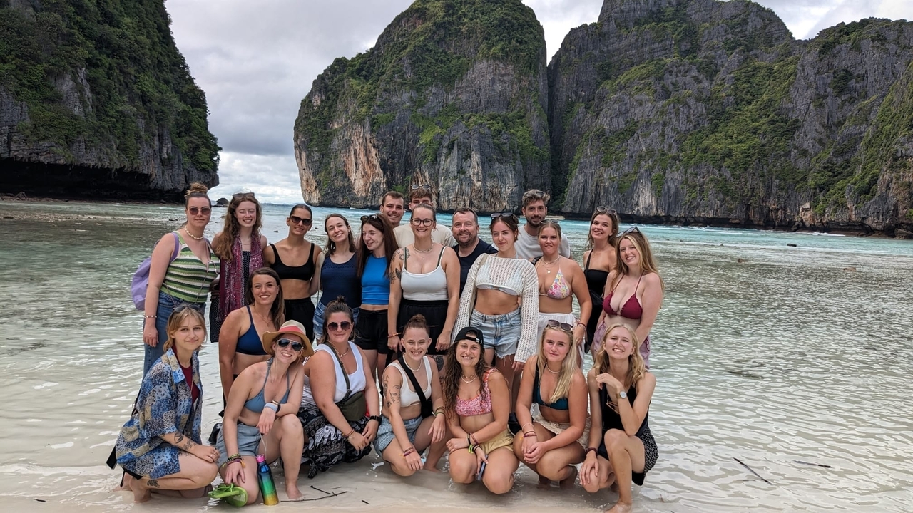 Grupo de personas en una playa con acantilados al fondo.