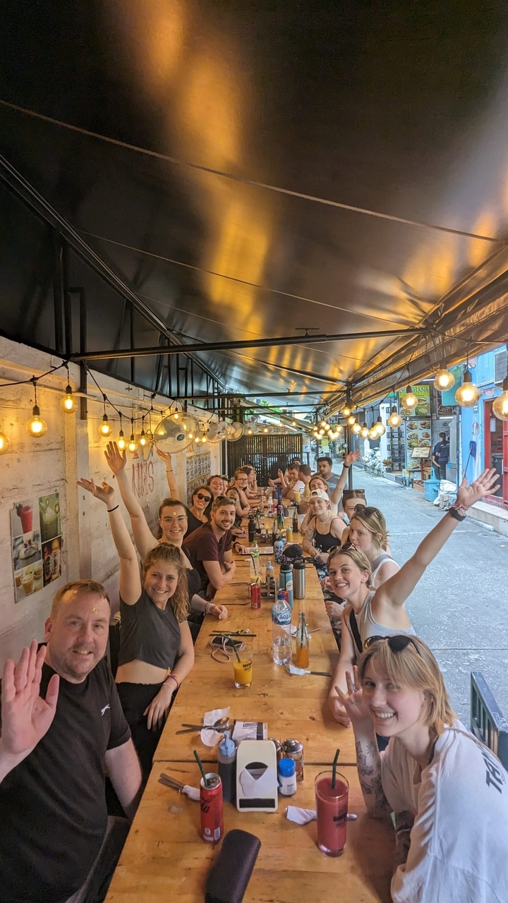 Grupo de personas cenando juntas bajo luces decorativas.