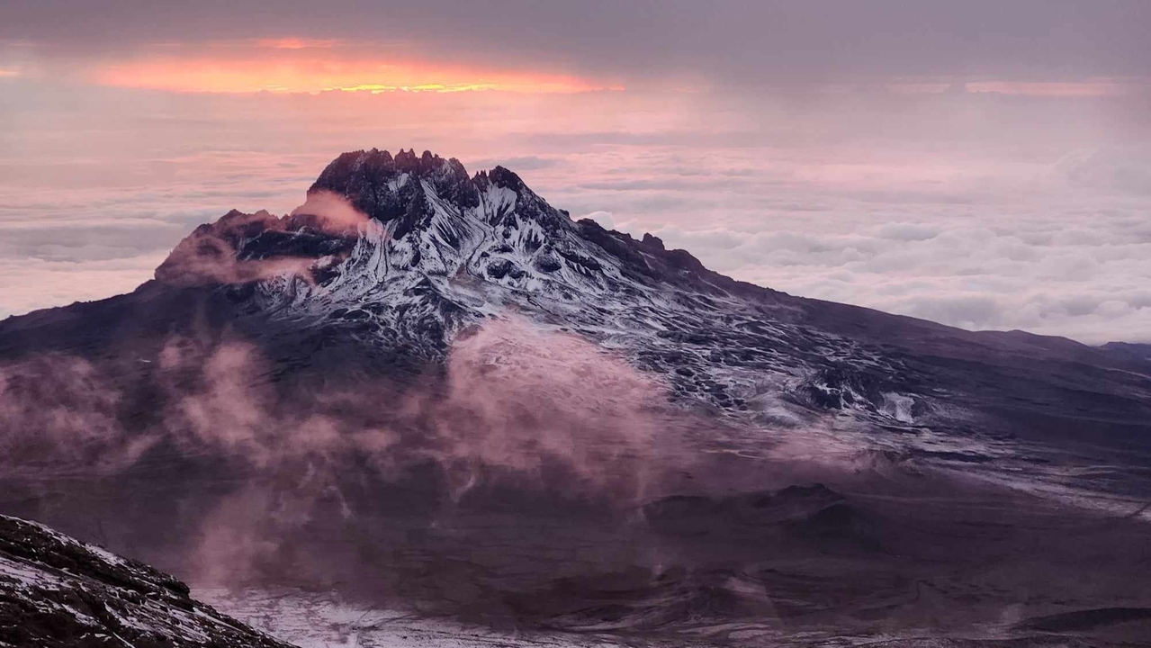 Pic de montagne entouré de nuages au coucher du soleil.