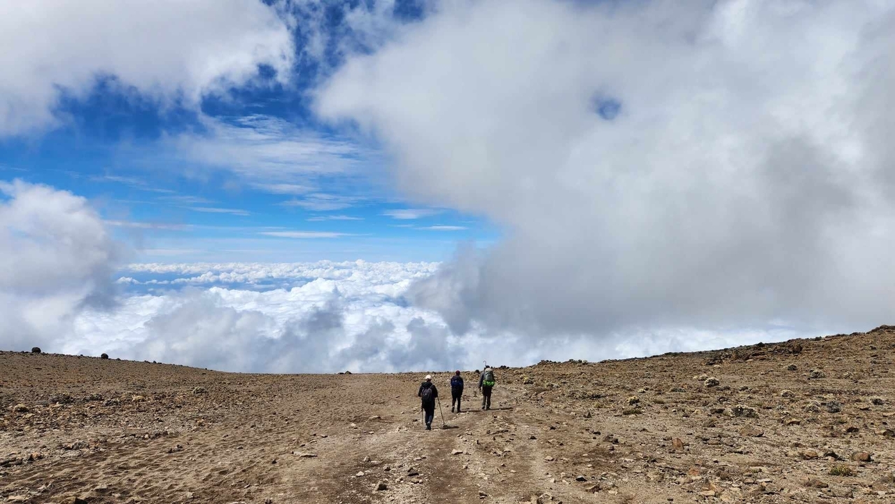 Trois personnes marchant le long d'un sentier montagneux au-dessus des nuages.