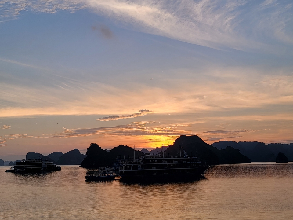 Coucher de soleil sur la baie d'Halong avec des bateaux en silhouette.