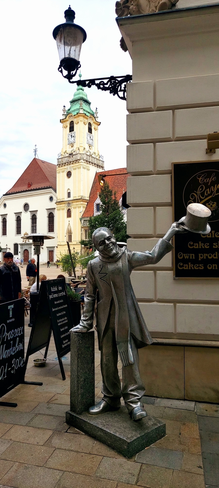 Statue tenant un chapeau devant un café de rue.
