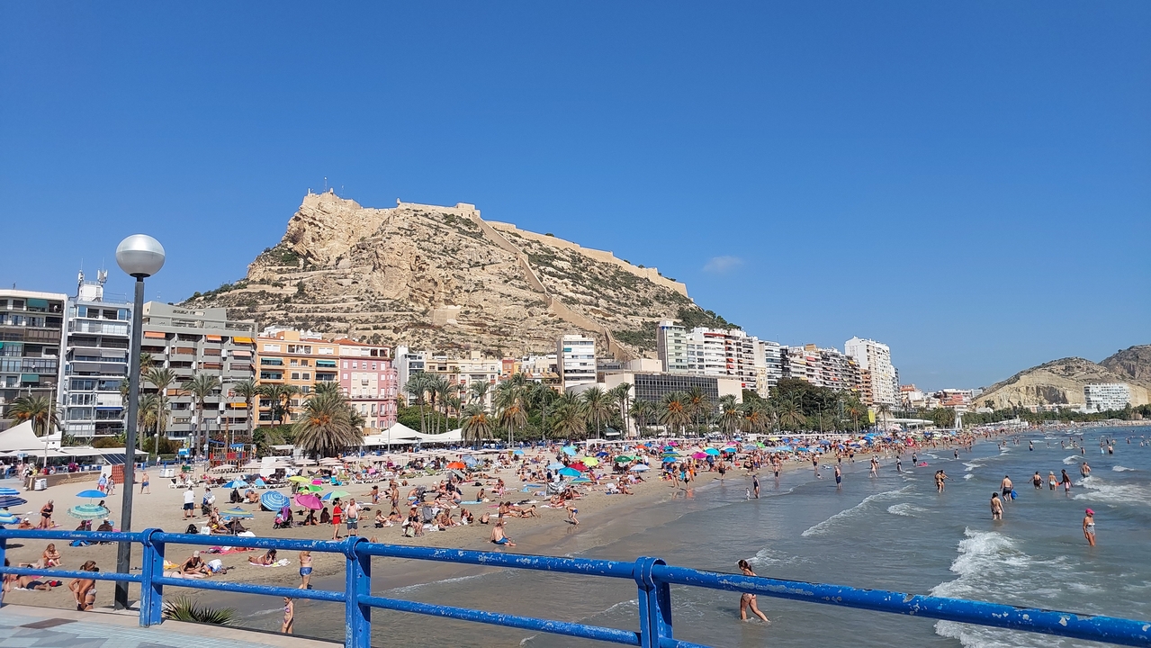 Scène de plage animée avec une falaise et des bâtiments urbains en arrière-plan.