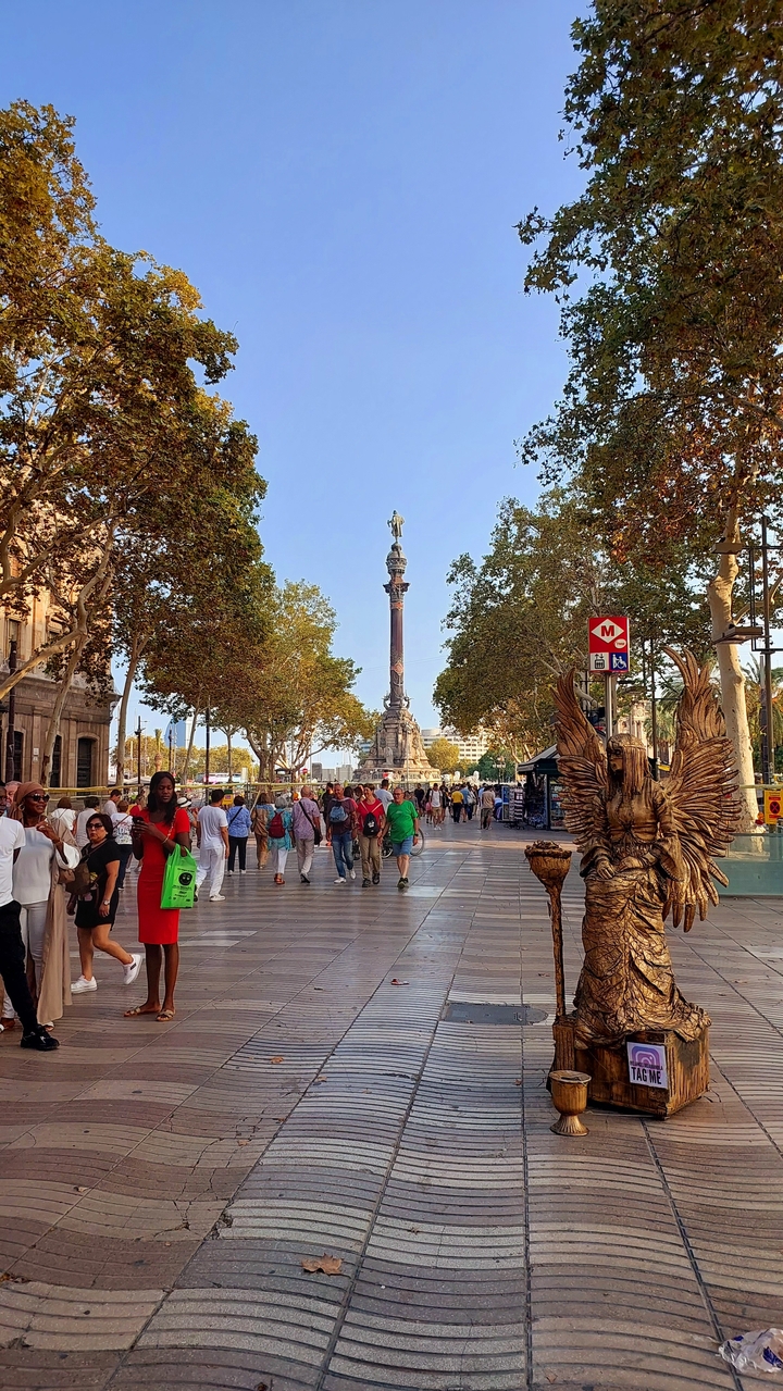 Scène de rue avec un monument en colonne et beaucoup de monde.