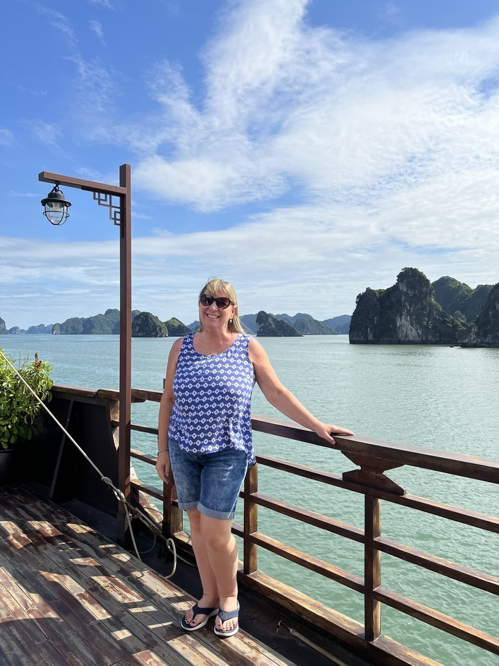 Femme souriante sur un bateau avec des îles rocheuses en arrière-plan.