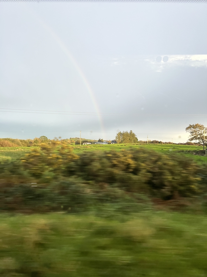 Vue depuis un véhicule en mouvement d'un arc-en-ciel au-dessus d'un paysage de campagne.