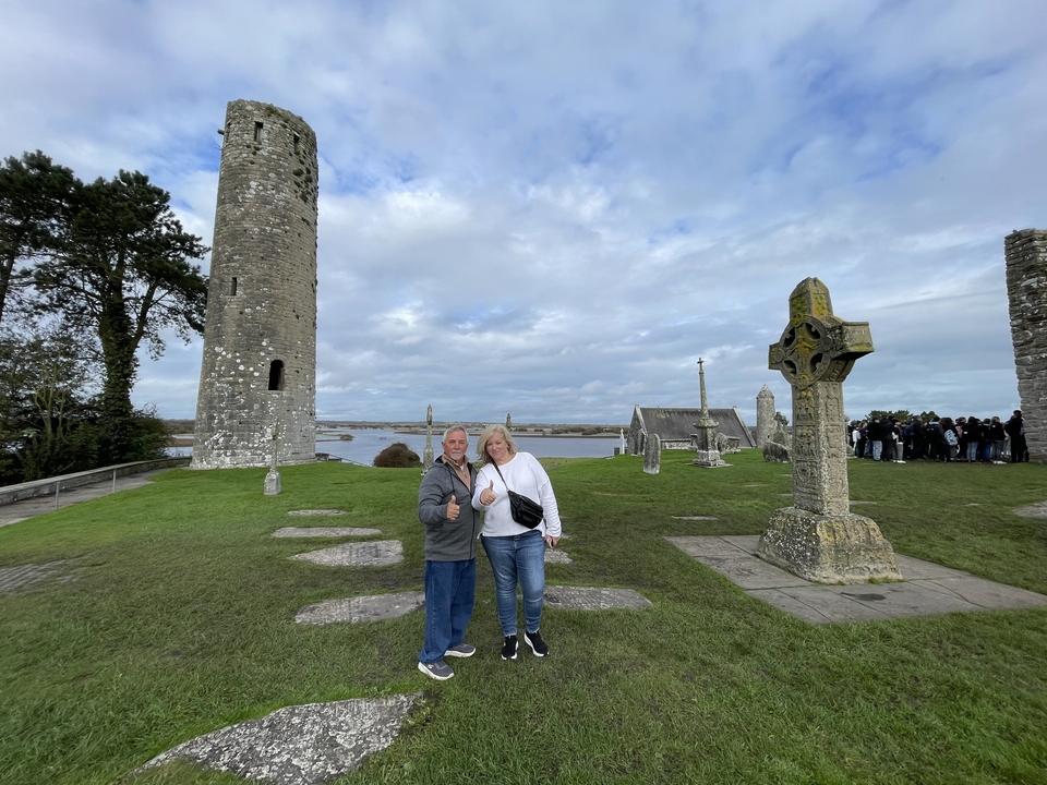 Un couple posant devant un site monastique avec une tour ronde et des croix de pierre.