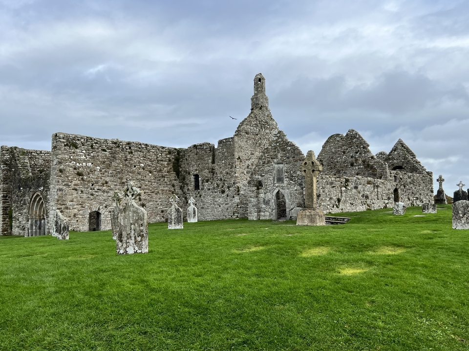 Anciennes ruines de pierre avec des pierres tombales sur une herbe verte luxuriante.