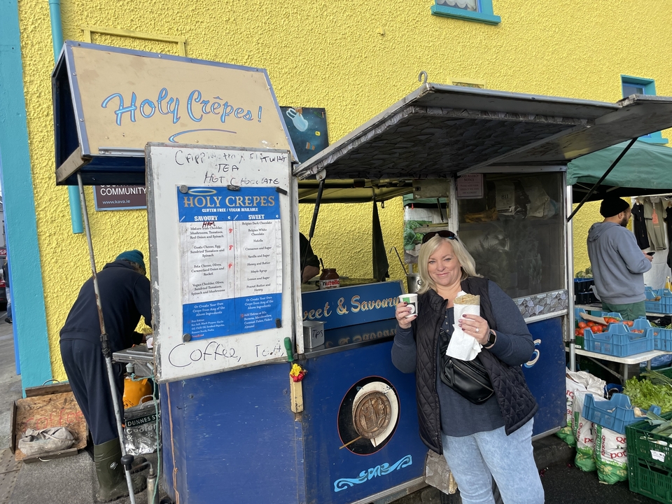 Une femme tenant une crêpe devant un étal de marché.
