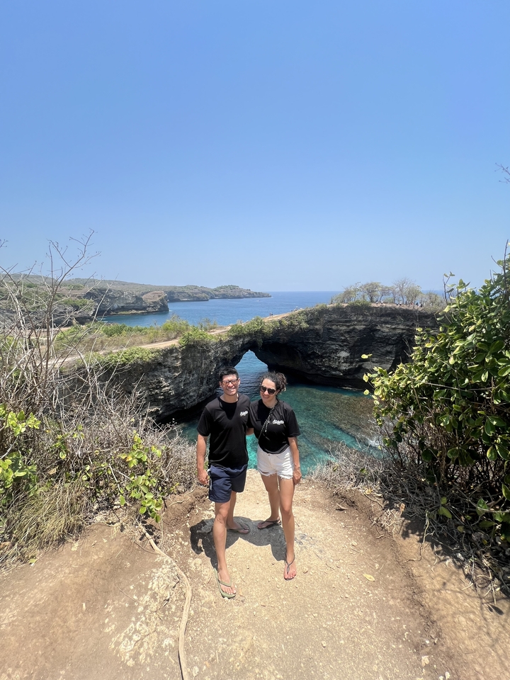 Couple posant devant une arche naturelle au-dessus de l'eau.