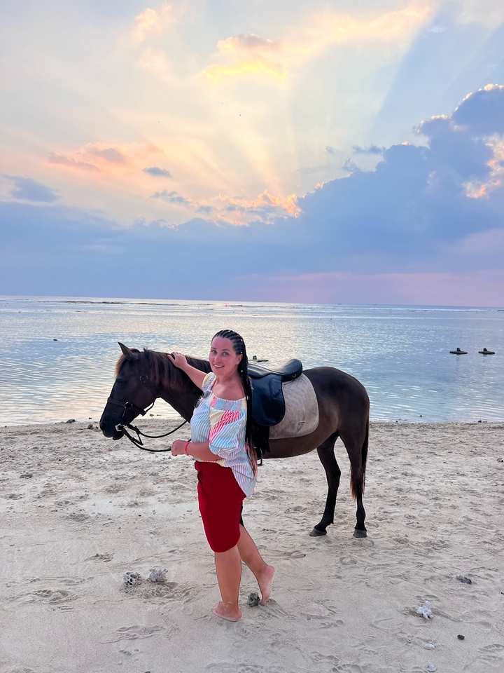 Femme debout avec un cheval sur une plage au crépuscule.