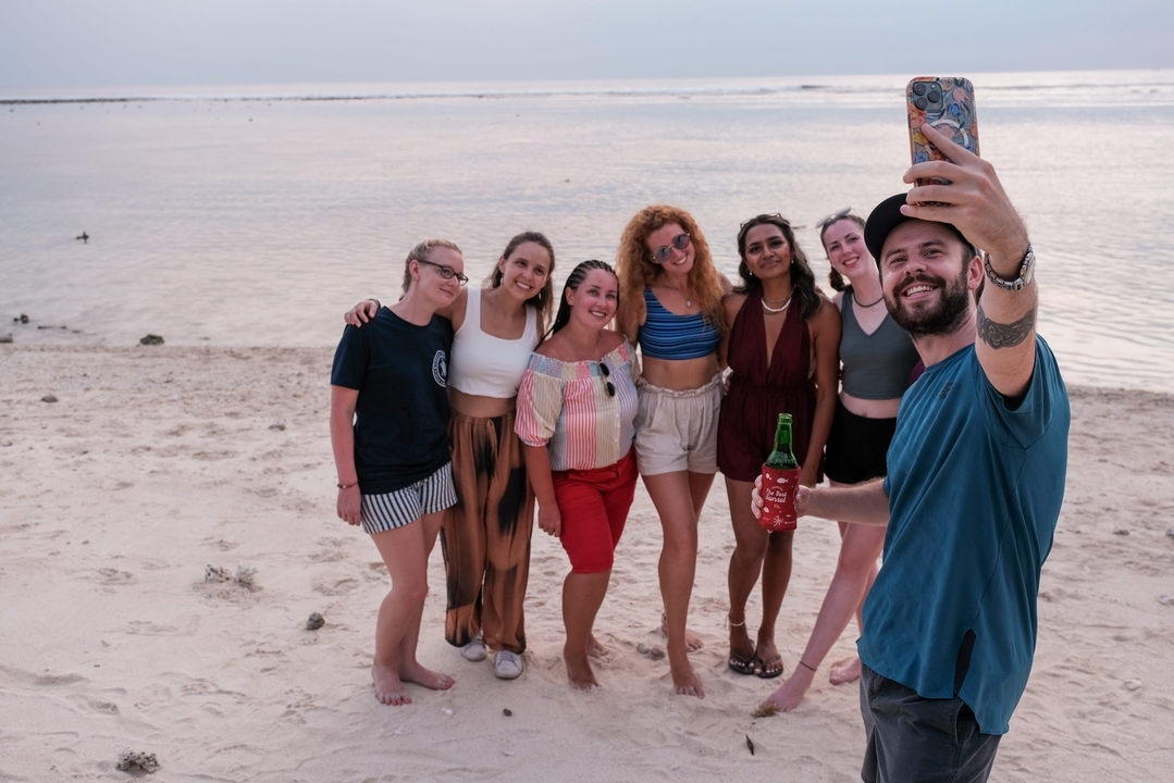 Groupe prenant un selfie sur une plage au coucher du soleil.