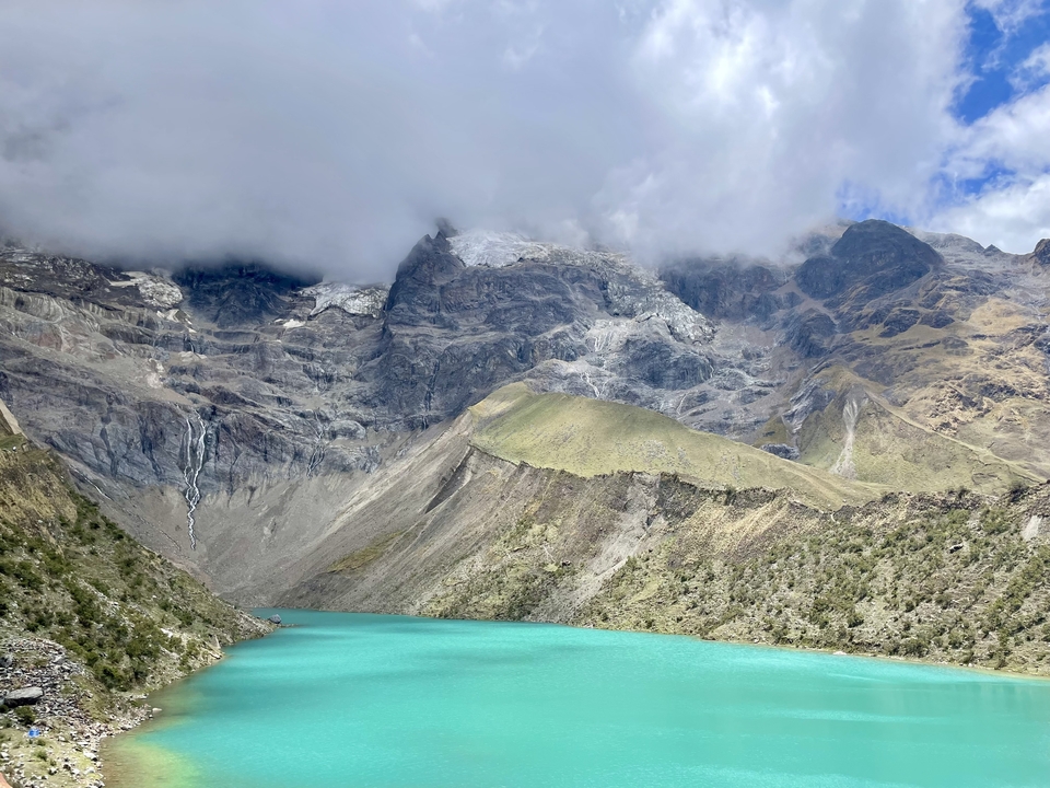 Lac turquoise entouré de montagnes rocheuses et de nuages.